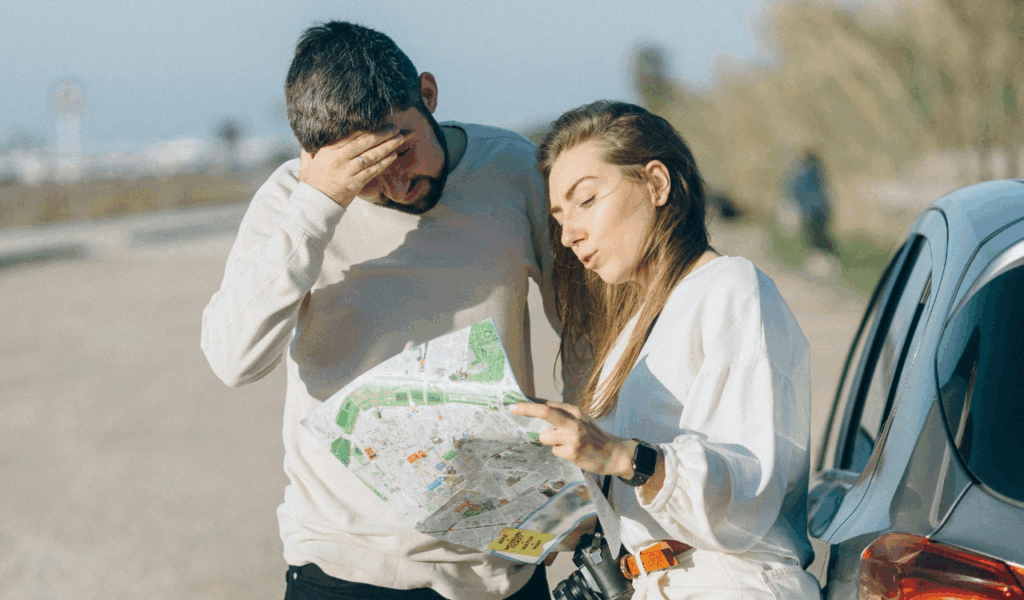Couple standing next to car outdoors, confused while reading a paper map, unsure of directions or next steps.