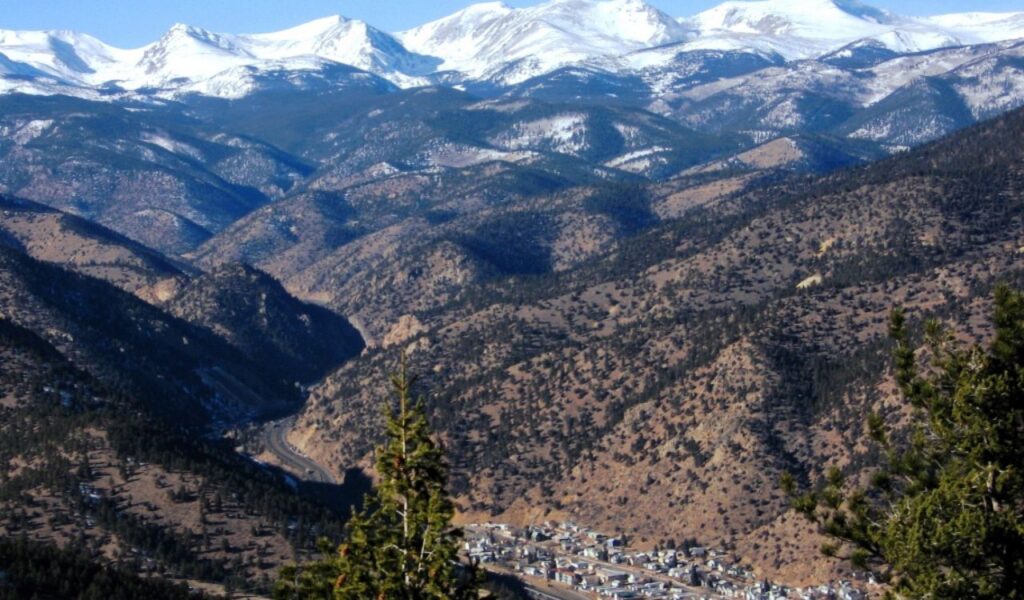 Idaho City nestled in forested valley with snowy mountain peaks in background.