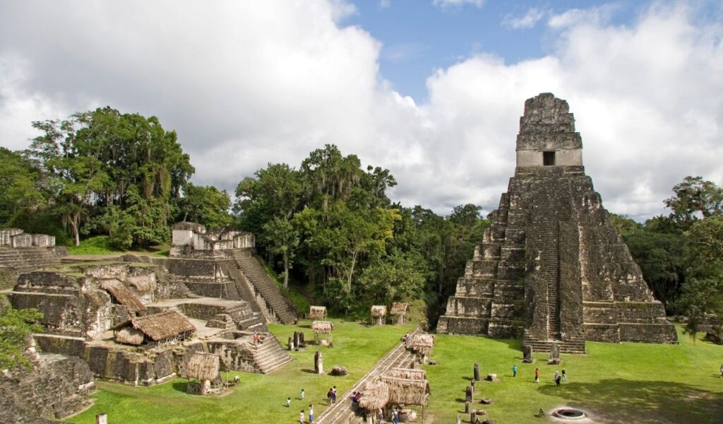 Tikal Temple I in Guatemala, a stepped Mayan pyramid rising above jungle ruins, with tourists exploring the site.