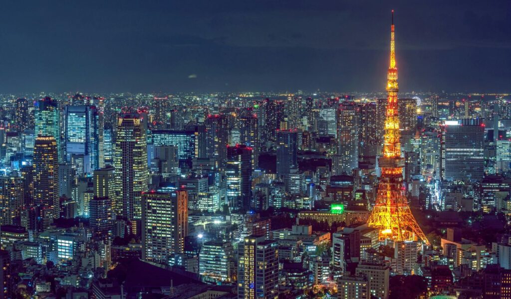 Night view of Tokyo with illuminated Tokyo Tower surrounded by skyscrapers and a sprawling cityscape filled with lights.