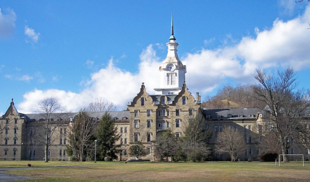 The Trans Allegheny Lunatic Asylum in Weston, West Virginia, a large historic stone building with a tall white clock tower under a blue sky.