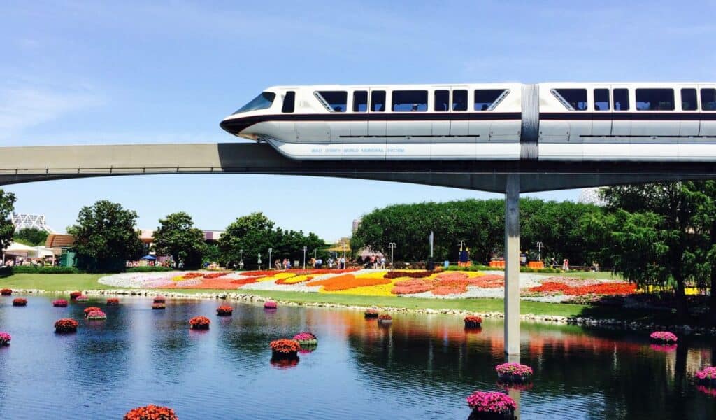 Disney World monorail gliding over a flower garden and pond on a sunny day, part of the park's transport system.