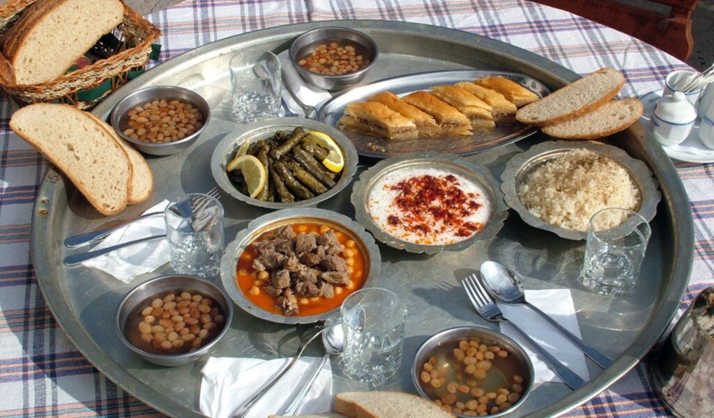 Traditional Turkish street food platter featuring grape leaves, baklava, chickpea stew, yogurt dip, and fresh bread served outdoors