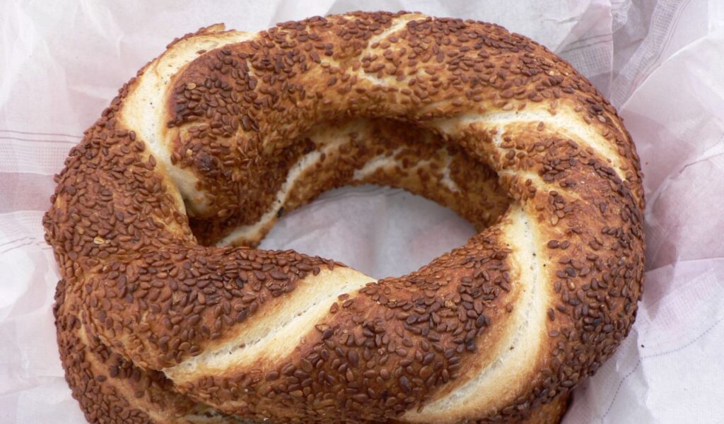 Close-up of a circular Turkish simit bread covered in toasted sesame seeds, placed on paper wrapping, ready to eat.