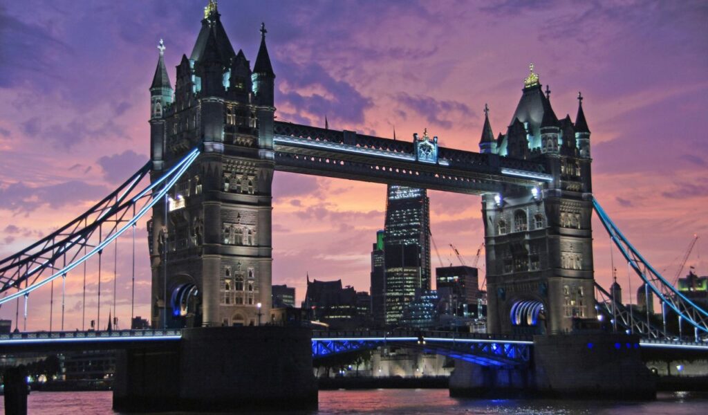 Tower Bridge in London illuminated at dusk with a vibrant purple and orange sky in the background.