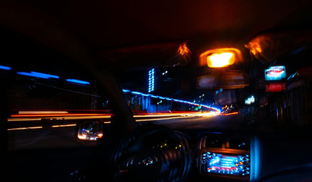 A car interior at night with interior lights on, showing blurred city lights outside through the windshield, illustrating night driving.