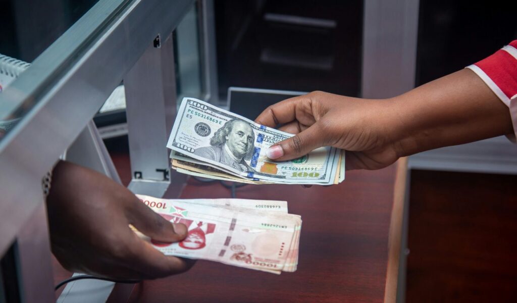 A close-up of hands exchanging U.S. dollars for foreign currency at a bank or currency exchange booth counter.
