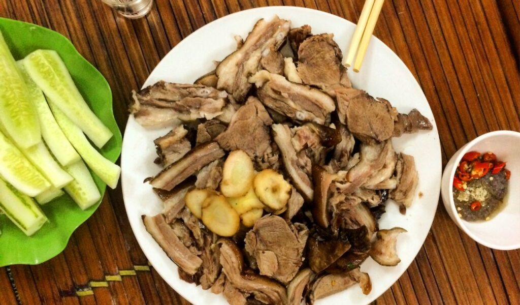 Traditional Vietnamese street food featuring boiled pork slices with garlic, chili dipping sauce, and fresh cucumber sticks