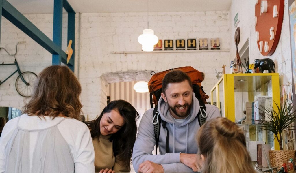 A cheerful couple with a backpack speaks to a travel agent across a colorful desk in a cozy, decorated office.