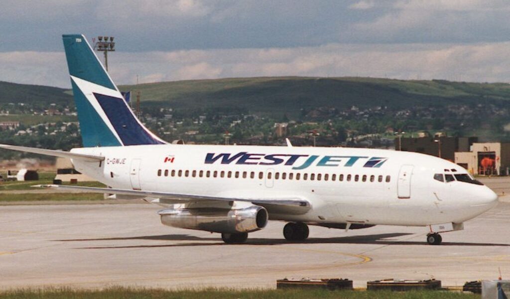 WestJet aircraft taxis at a Canadian airport, featuring its teal and blue tailfin and maple leaf insignia.