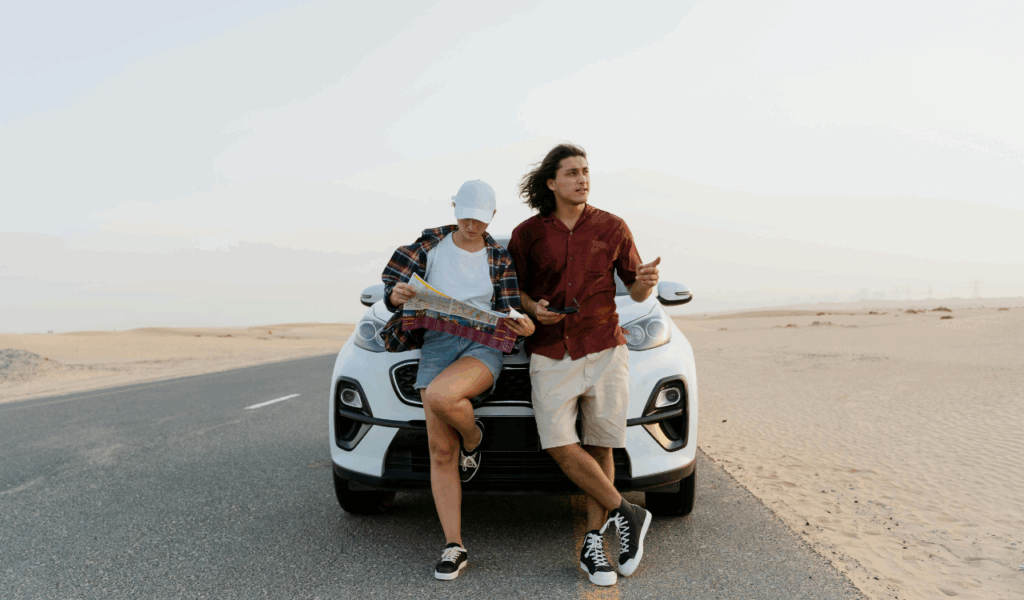 Couple planning their road trip while sitting on a white car in a desert, reviewing a map and discussing directions.