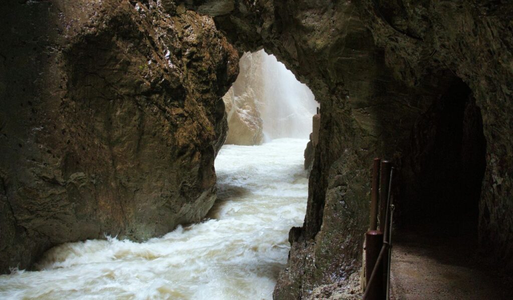 Rushing water flows through the narrow rocky passage of Partnach Gorge, with steep cliffs and a walkway carved into the stone