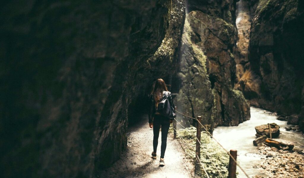 A person walking along a narrow path inside Partnach Gorge with steep rocky walls and a flowing river beside them.
