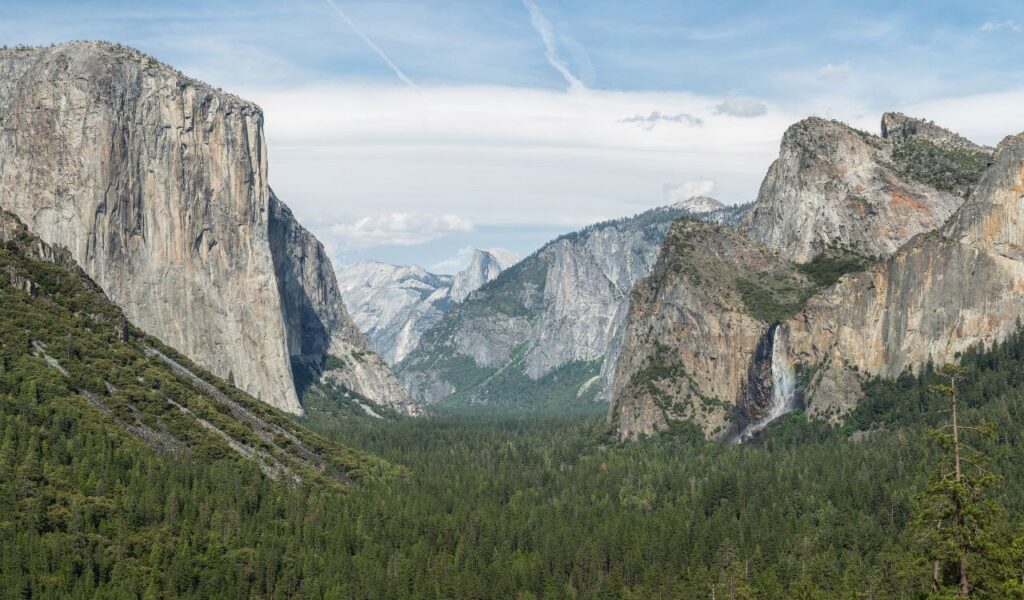 View of Yosemite Valley with El Capitan, Bridalveil Fall, and Half Dome rising above dense forest in Yosemite Park.