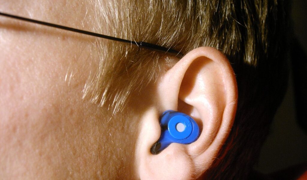 Close-up of a person's ear wearing a blue earplug, showing detail of the plug's shape and position for noise protection.