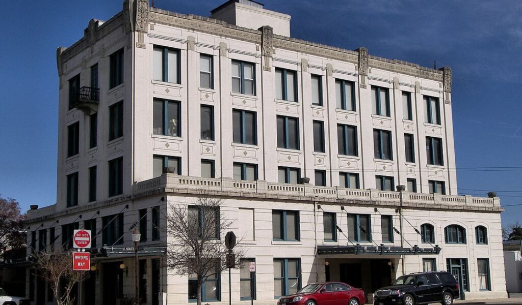 Historic multi-story white brick building with large windows and decorative stonework in downtown Seguin, Texas, under a clear blue sky.