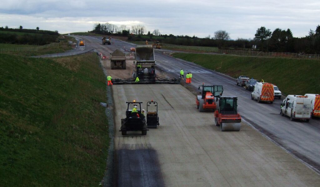 Road construction in progress with workers and heavy machinery, emphasizing the need to adjust driving to road conditions.