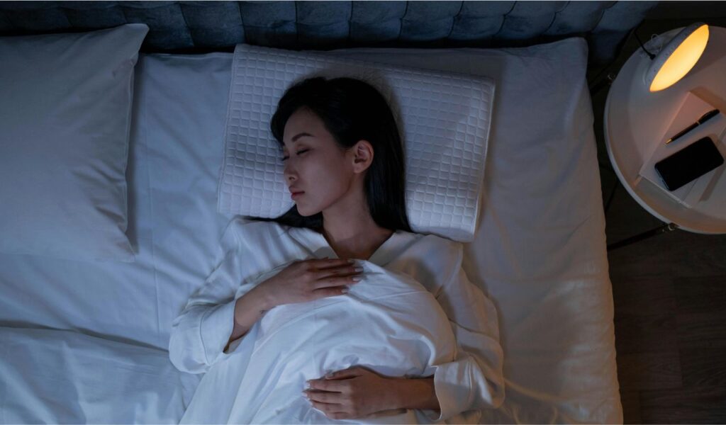 Woman peacefully sleeping in a dimly lit bedroom, adjusting her sleep schedule before an upcoming long-haul flight.