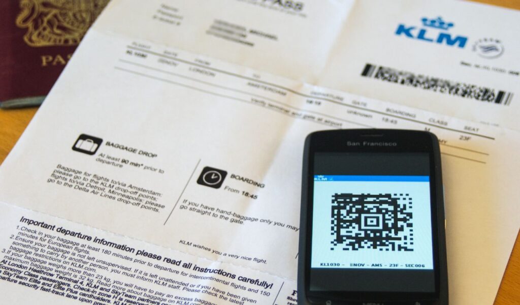 Printed boarding pass and mobile phone displaying a KLM boarding pass QR code next to a passport.