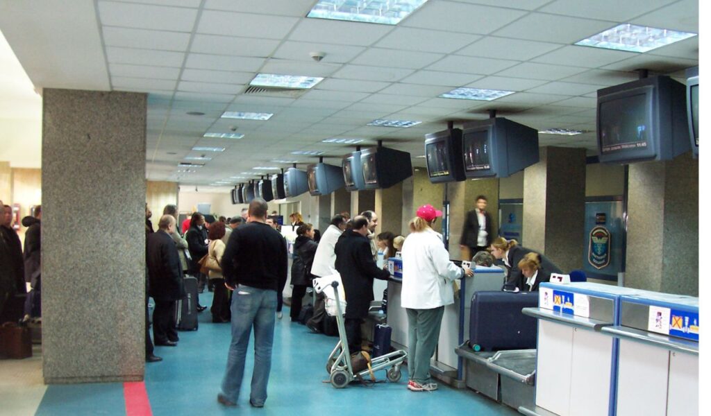 Travelers lined up at an airport check-in counter, some with luggage carts—highlighting potential baggage fees.