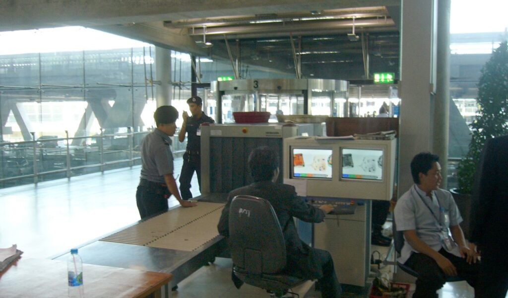 Airport security checkpoint with staff monitoring x-ray machines and luggage being processed on the conveyor belt.