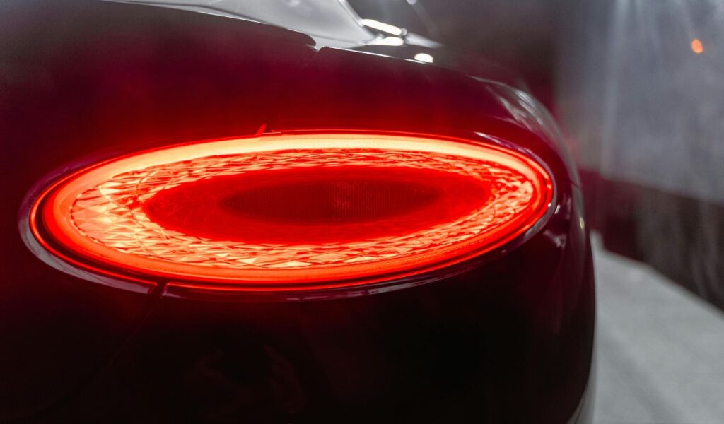 Close-up view of a car’s illuminated rear turn signal light glowing bright red in a dark environment.