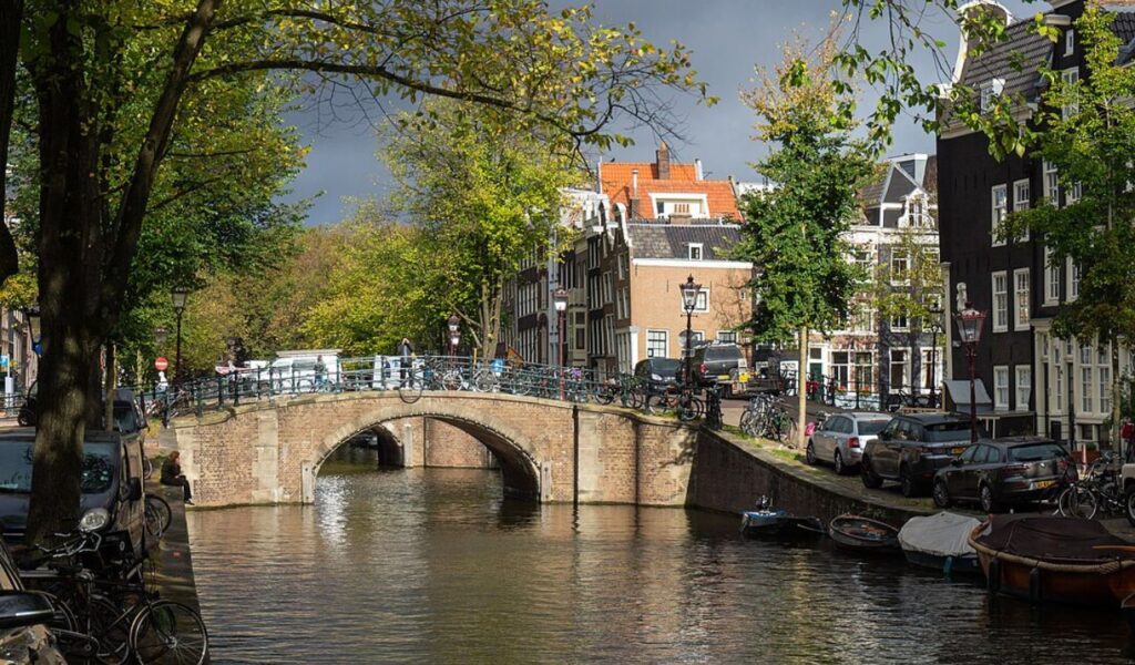 Stone bridge over canal with bikes and historic houses in Amsterdam.