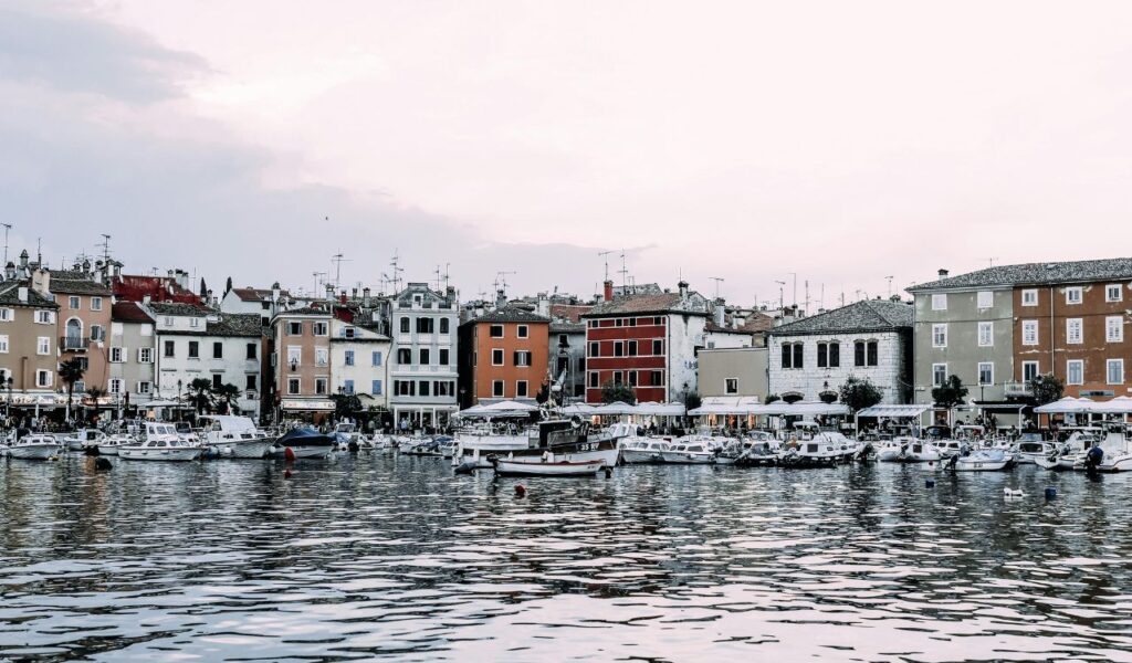 Colorful waterfront buildings and docked boats in a small European coastal town, showing a quiet travel destination.