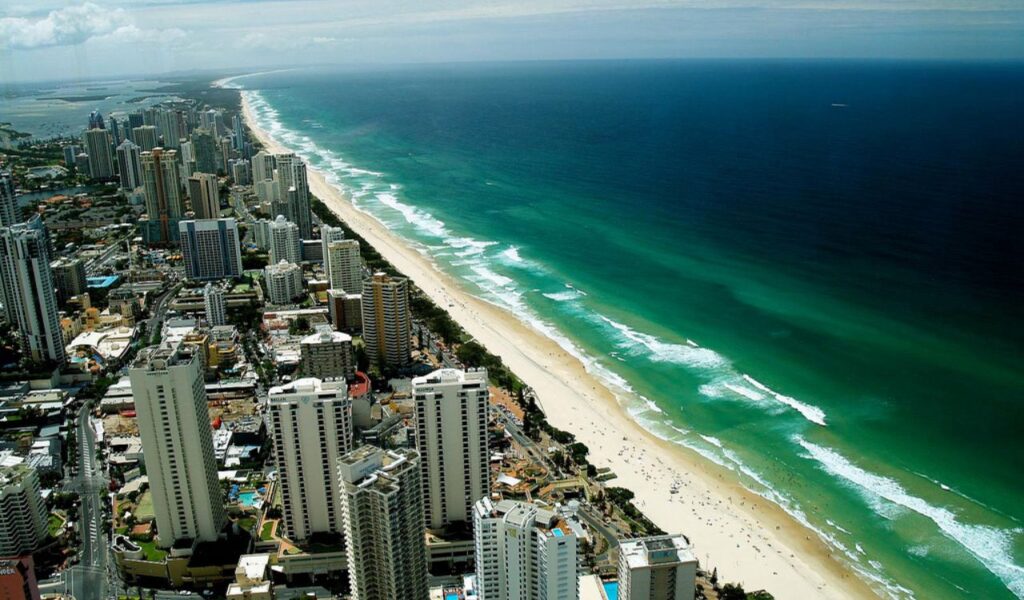 Panoramic view of a coastal city with towering skyscrapers alongside a beautiful sandy beach and turquoise ocean.