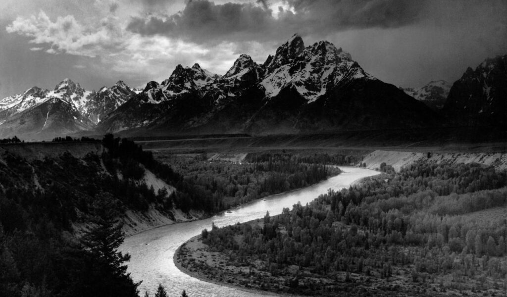Snake River winding through forested valley with snow-covered Teton mountains in the background.