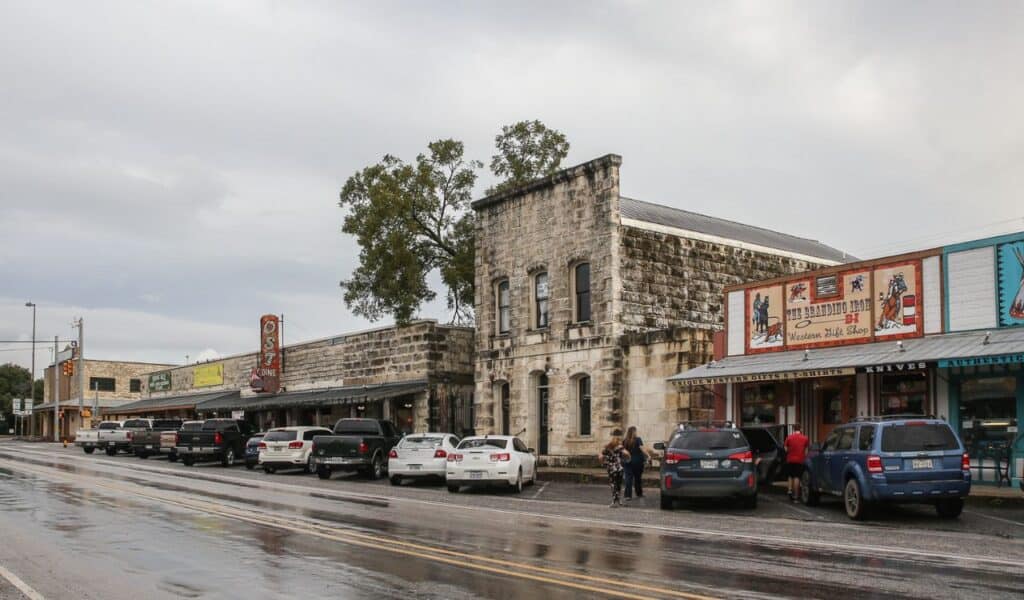 View of downtown Bandera, Texas, with stone buildings, Western-themed shops, parked cars, and wet roads after rain.