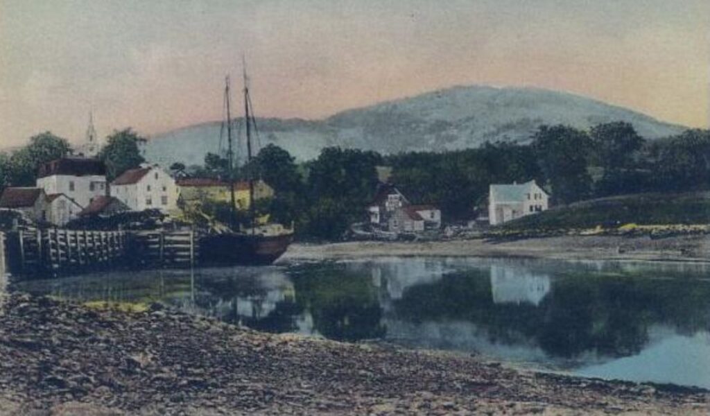 Vintage postcard view of Blue Hill, Maine with docked sailboat, historic buildings, and forested hills in the background.