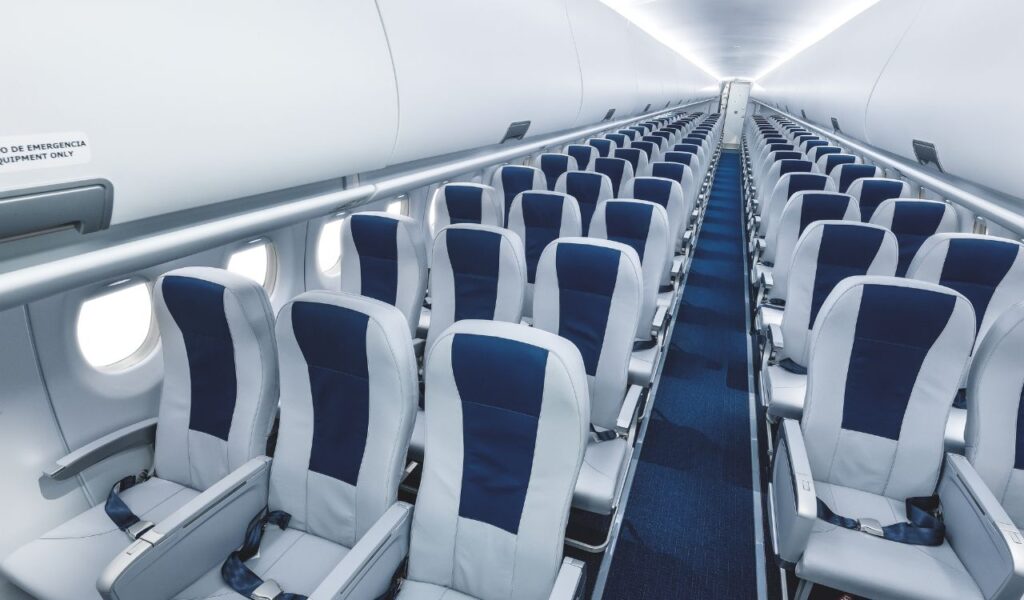 Empty airplane cabin with rows of blue and white economy seats, viewed from the rear toward the front, during daylight.