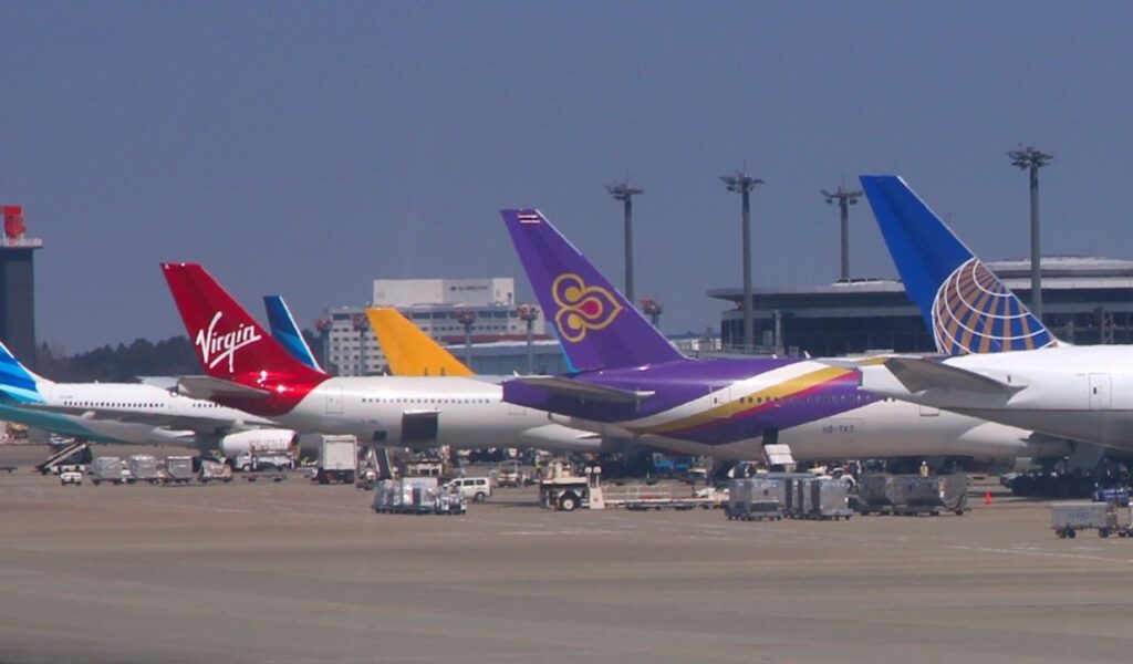 Multiple international airline planes from different carriers, including Virgin, Thai Airways, and United Airlines, parked at airport gates, representing diverse flight options.
