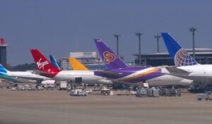 Multiple international airline planes from different carriers, including Virgin, Thai Airways, and United Airlines, parked at airport gates, representing diverse flight options.