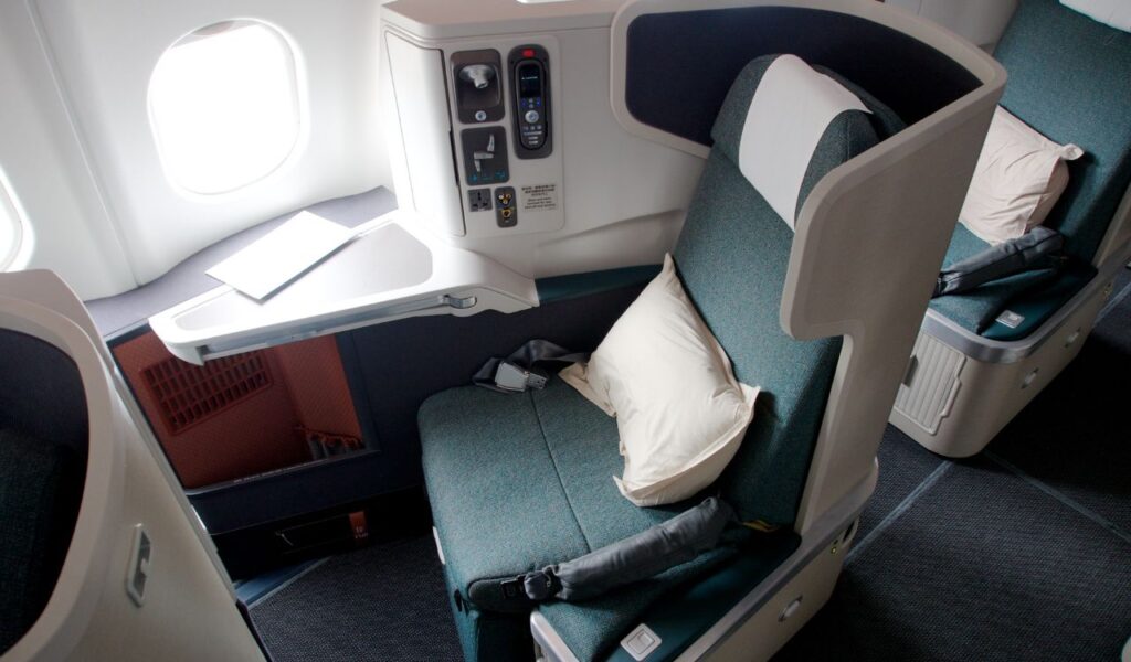 Spacious business class airplane seat with pillow, personal screen, and control panel, designed for long-haul comfort.
