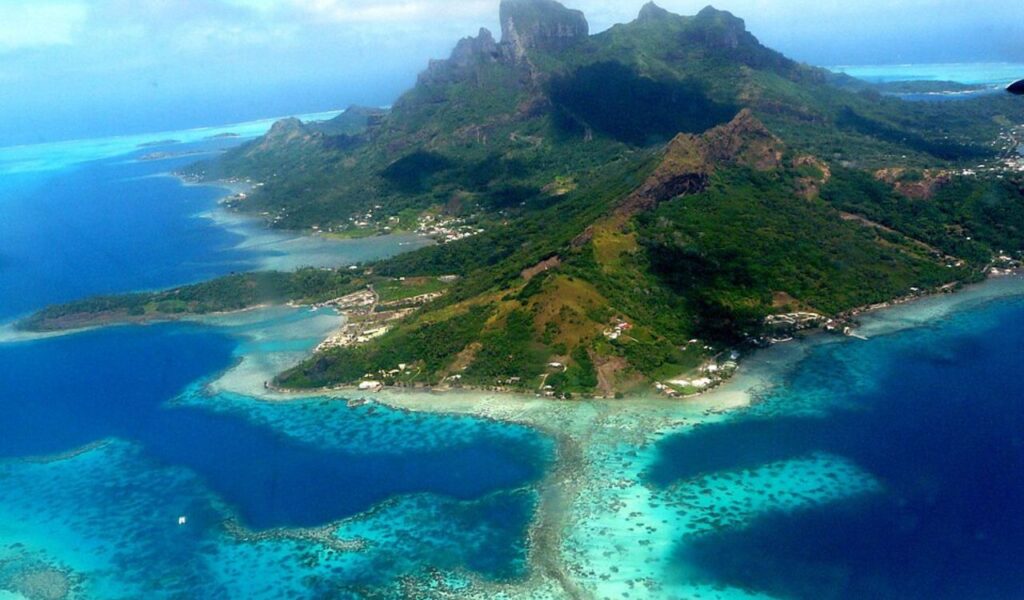 Aerial view of Bora Bora with lush volcanic peaks, turquoise lagoons, coral reefs, and scattered coastal villages.
