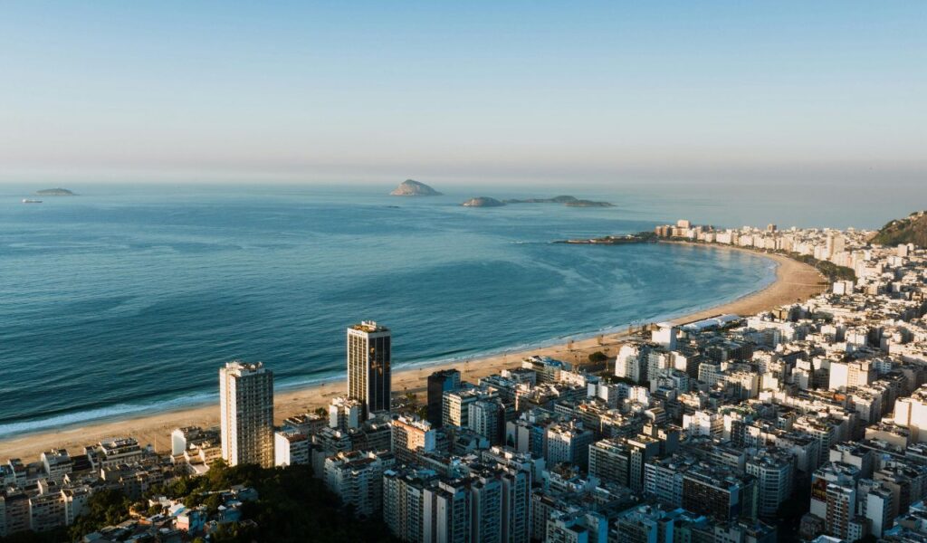 Aerial view of Rio de Janeiro, Brazil, featuring Copacabana Beach curving along the coastline with high-rise buildings and small islands in the distance under a clear sky.