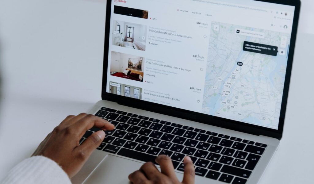 A person using a laptop to browse accommodation listings on a travel booking site with a map view on the side.