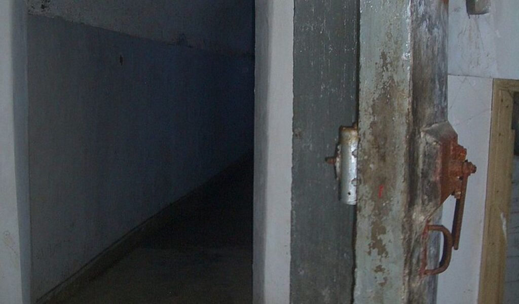Rusty metal blast door leading into a dim hallway inside the Burlington Bunker, a Cold War-era underground facility in England.