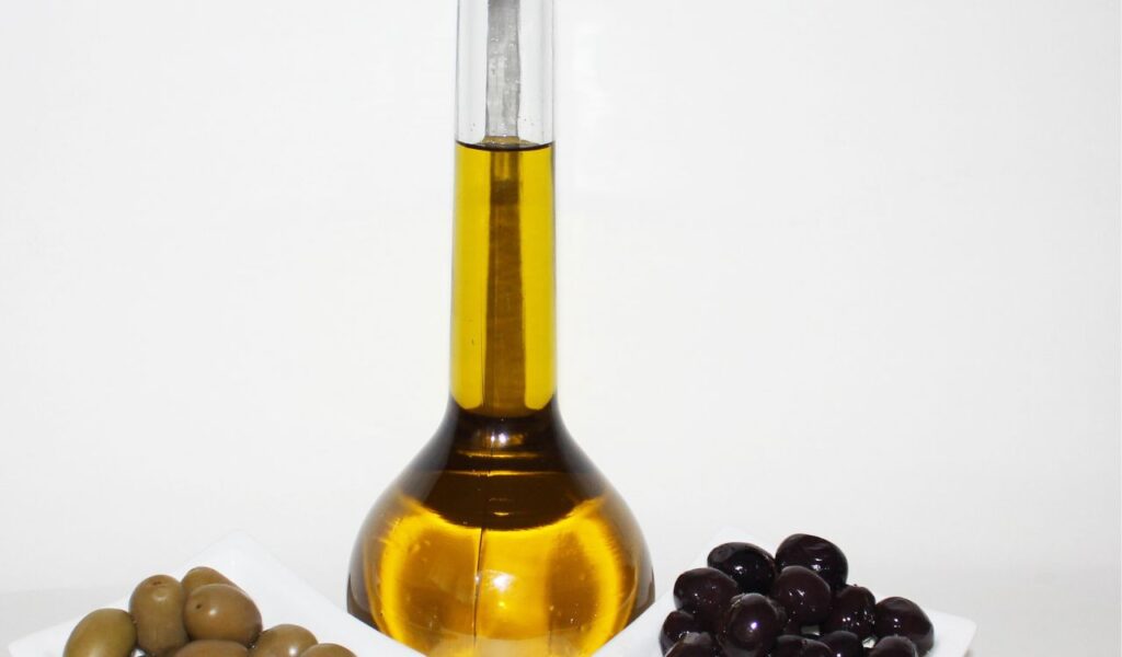 Bottle of olive oil flanked by bowls of green and black olives, representing traditional Greek food products.