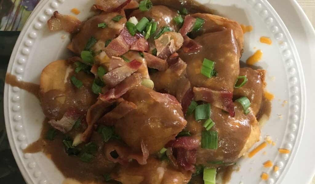 A plate of Canadian poutine topped with gravy, cheese curds, bacon pieces, and chopped green onions, served on white dish.