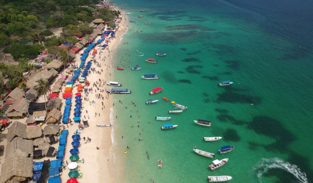 Aerial view of a colorful beach in Cartagena, Colombia, with vibrant umbrellas, thatched huts, and boats floating in turquoise water.
