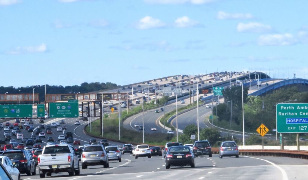 Heavy traffic crossing the Driscoll Bridge on a sunny day, with green highway signs pointing to Perth Amboy and I-95 North.