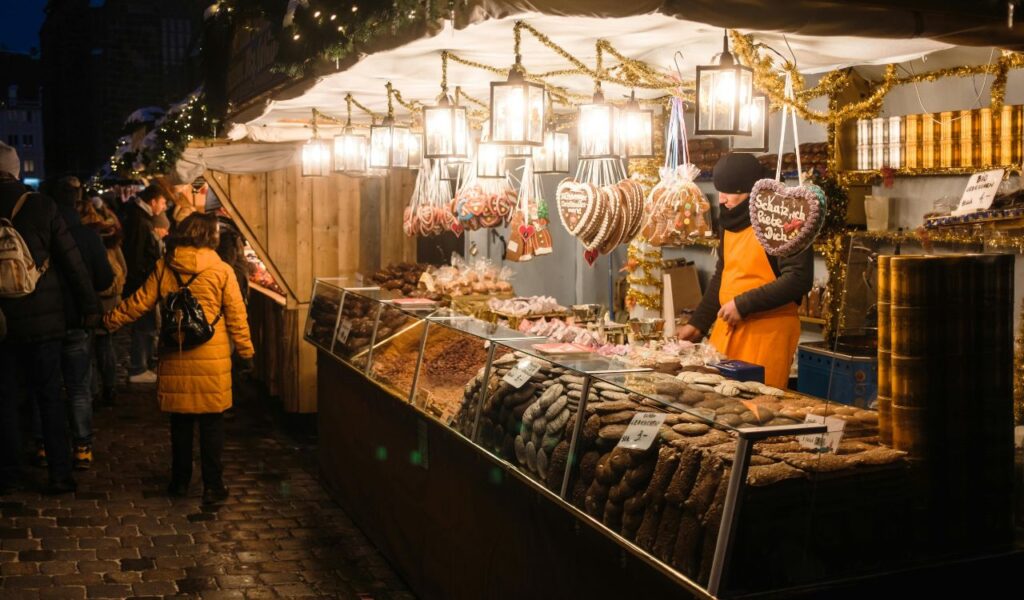 Festive food stall at Nuremberg’s Christkindlesmarkt, with gingerbread cookies, nuts, and sweets on display under warm hanging lights and holiday decorations.