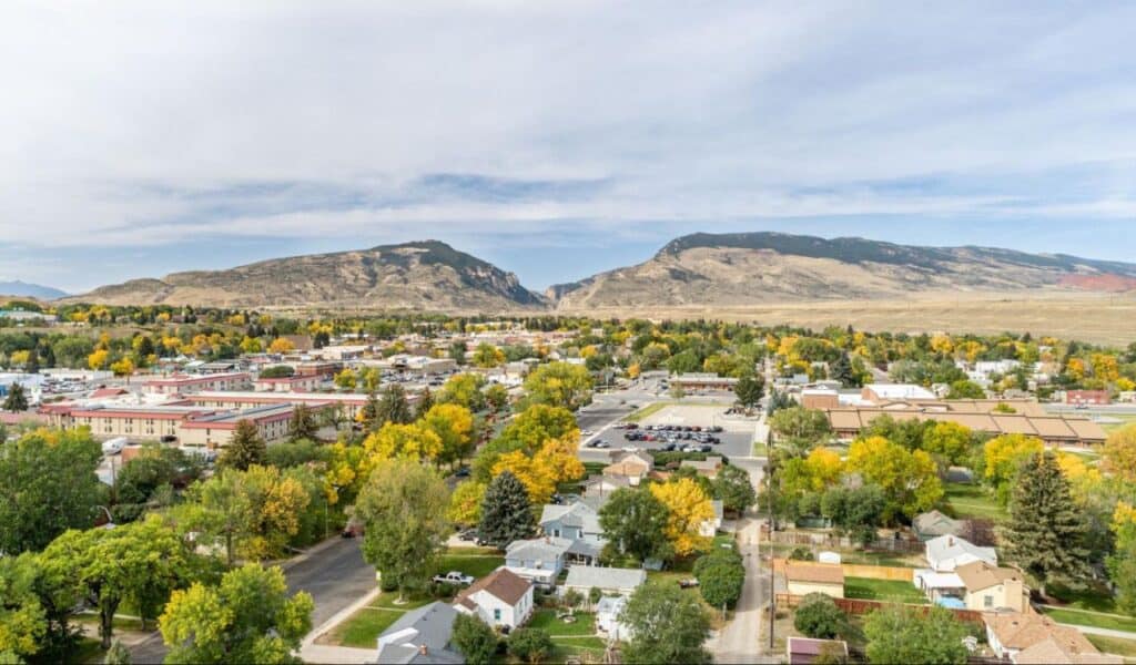 Aerial view of Cody, Wyoming, with colorful trees, small-town homes, and rugged mountain backdrop.