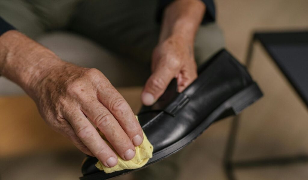 Person polishing a black leather shoe with a yellow cloth, showing care and maintenance of footwear up close.