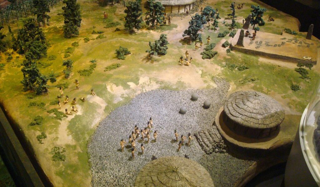 Miniature diorama depicting an ancient village in Costa Rica with thatched huts, trees, and small human figures engaging in daily life.