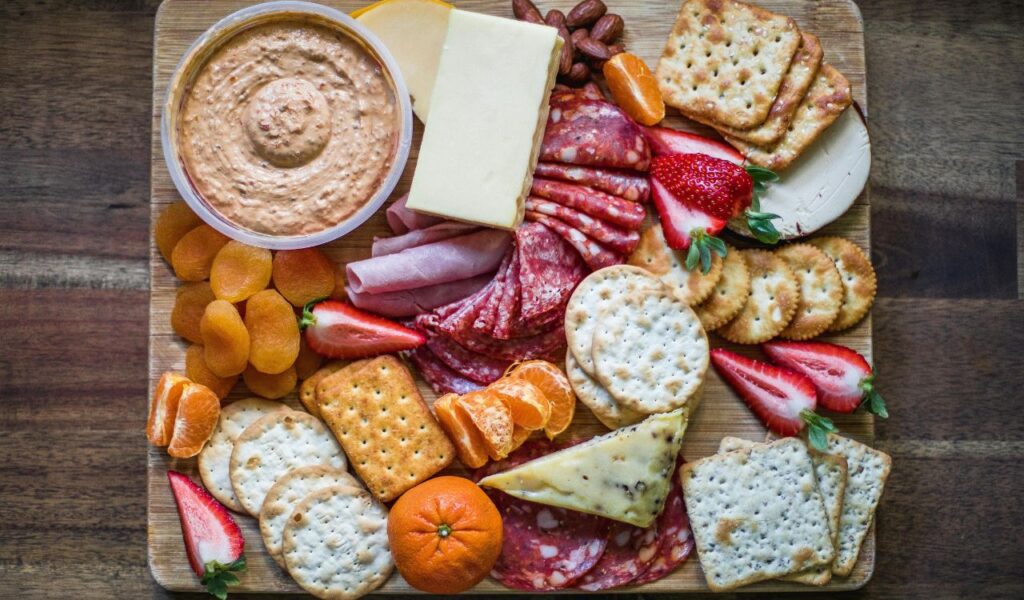 A charcuterie board from Cracker Barrel featuring assorted crackers, cheese, cured meats, strawberries, tangerines, dried apricots, almonds, and a bowl of dip.