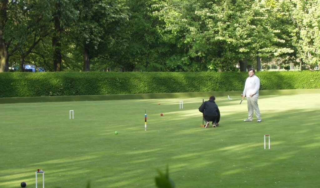 A serene scene of two people playing croquet on a well-maintained lawn, with colorful balls and wickets set up for the game.